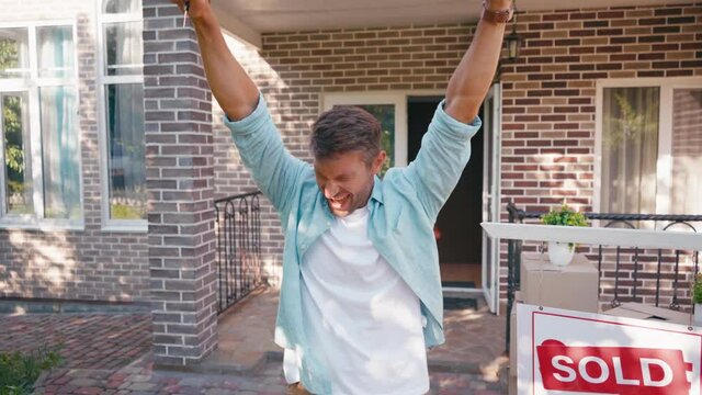 excited man pointing with hands at new house, screaming and jumping outside