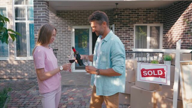 man pouring wine in glass of woman near sold board and new house