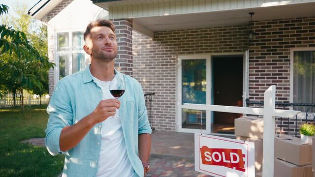 joyful man holding glass of wine and looking at new house