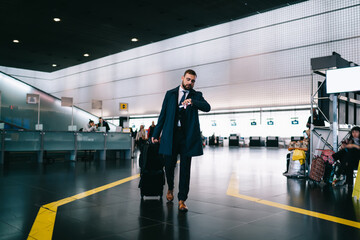 Caucasian businessman checking time on modern smartwatch hurry up to airport gate in terminal, formally dressed commuter with luggage suitcase using wearable wrist clock during work travelling - Powered by Adobe