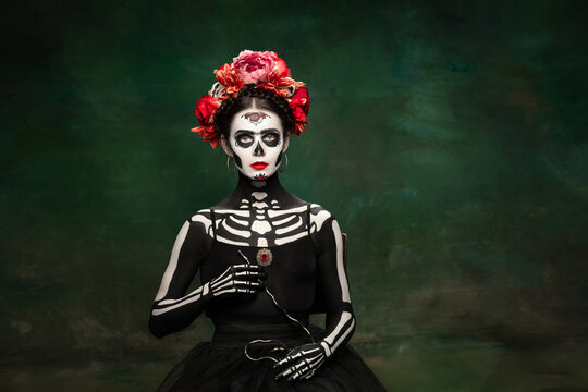 Poison. Young girl like Santa Muerte Saint death or Sugar skull with bright make-up. Portrait isolated on dark green studio background with copyspace. Celebrating Halloween or Day of the dead.