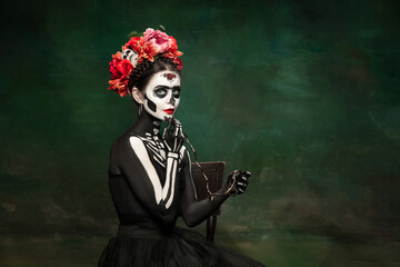 Poison. Young girl like Santa Muerte Saint death or Sugar skull with bright make-up. Portrait isolated on dark green studio background with copyspace. Celebrating Halloween or Day of the dead.