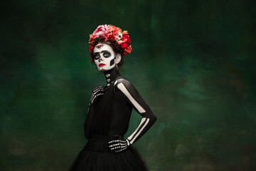 Fototapeta na wymiar Poison. Young girl like Santa Muerte Saint death or Sugar skull with bright make-up. Portrait isolated on dark green studio background with copyspace. Celebrating Halloween or Day of the dead.