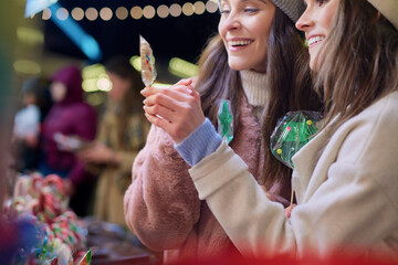 Naklejka premium Friends buying candies Christmas market at night