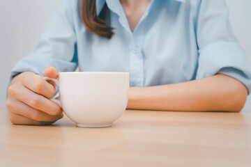 White hot coffee mug on the desk and female holding to drink on background.