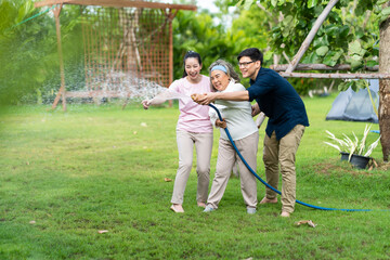 Fototapeta premium Asian family happy smiling and watering green cultivated plants with a garden hose at home. Happy family concept. 4 people father Mather sun daughter.