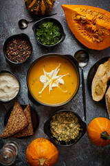 Delicious pumpkin soup with cream, seeds, bread and fresh herbs in elegant ceramic black bowl