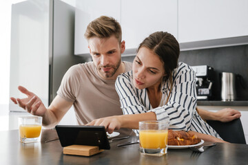 Young couple looking at cellphone while having breakfast at home