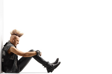 Pensive punk rocker with a mohawk sitting on the ground and leaning on a wall