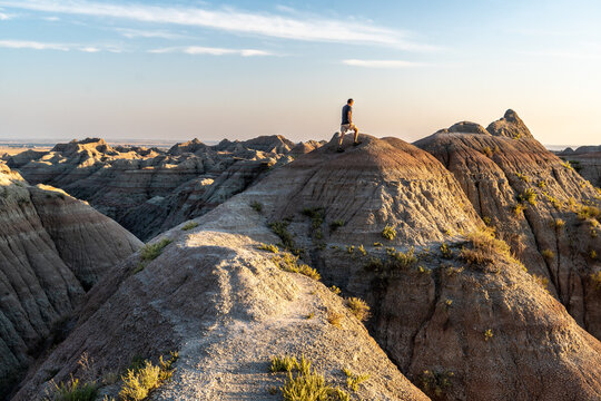 Man, Person, climbing to the top of a ridge of Striated rock, wispy cloud in the sky, Badlands National Park, South Dakota - Powered by Adobe