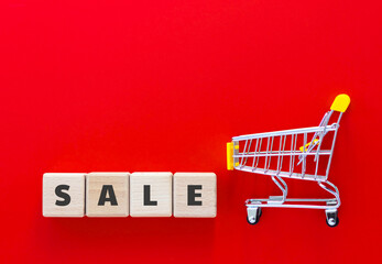Mini supermarket cart and wood cubes with text SALE on red background. Online shopping, business...
