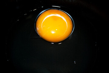 Broken raw egg in a black / dark gray plate. Cooking concept.