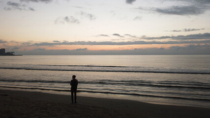 silhouette of a young guy standing by the sea coast, sunset, aerial photography