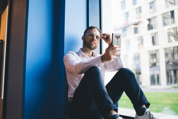 Handsome Caucasian man in eyeglasses installing network application for web socialising in online mode, millennial male blogger reading received smartphone message during content chatting and texting