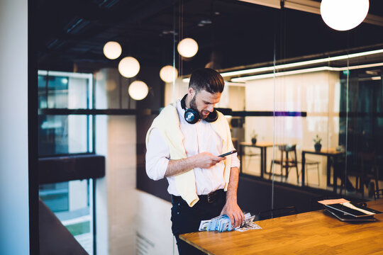 Smart casual coworker using cellphone device for checking income dividend during stock exchange during money making, Caucasian businessman with dollars wad writing email message about earnings