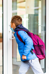 Obraz premium Back view of schoolboy is trying to open the school door. Behind the backpack look through the transparent door