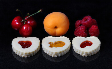 Christmas butter cookies with cherry and raspberry and apricot jam on black marble.