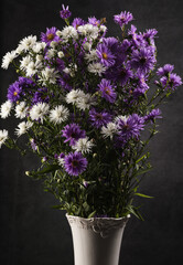 Bouquet of small garden asters in a white vase on a gray background.