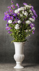 Bouquet of small garden asters in a white vase on a gray background.