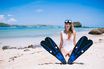 Pleased woman in mask and flippers for diving sitting on beach © BullRun