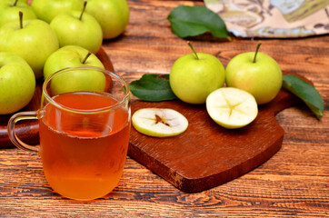 glass of fruit juice and apples on wooden background