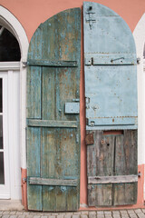 Altes Handwerk: Verwittertes blaues Holztor Fensterladen mit eisernen und rostigen Türbeschlägen vor apricot farbener Hauswand  