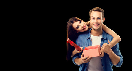 Love, relationship, dating, flirting, lovers, romantic concept - happy couple opening gift box, looking at camera. Isolated over black background. Copy space for some text.