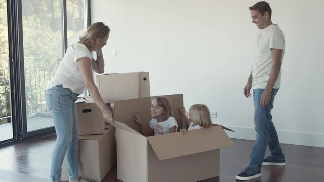 Parents opening big cartoon box with cheerful daughters inside. Family having fun while moving into new flat. Moving into new house concept