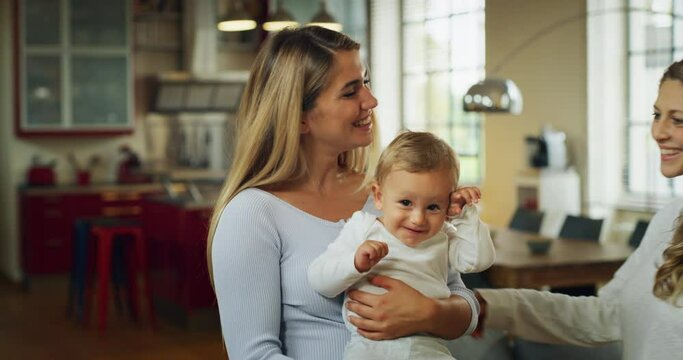 Authentic shot of young happy homosexual female gay family with son toddler baby boy is smiling in camera in a kitchen at home.