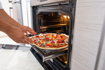 A young woman cook puts a blank vegan pizza in the oven.