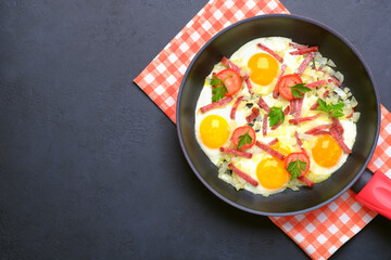 Fried eggs with tomatoes and sliced sausages in a frying pan on a black background