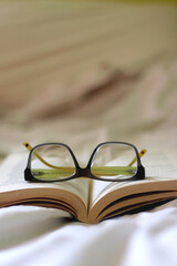 Open book and reading glasses on a bed. Selective focus.