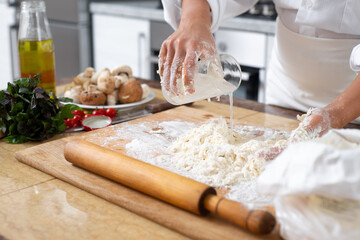 The cook pours water from a glass into the dough lying on the table.