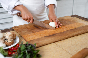 Close-up, a cook prepares to chop an onion. The photo shows the hands of the cook with an onion and a knife.