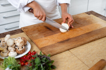 Close-up, the cook starts cutting the onion into rings with a knife.