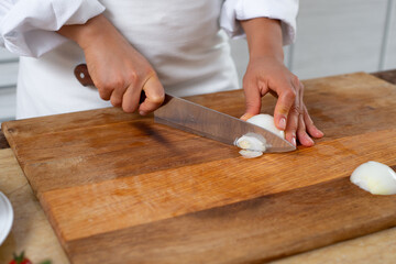 Close-up, the chef cuts the onion with a knife on a wooden board.