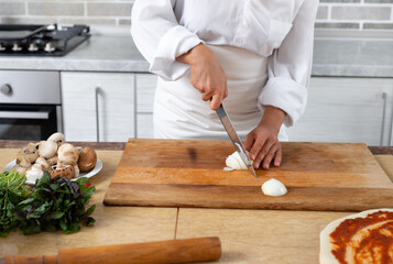 Close-up, the chef cuts the onion with a knife on a wooden board. Front view.