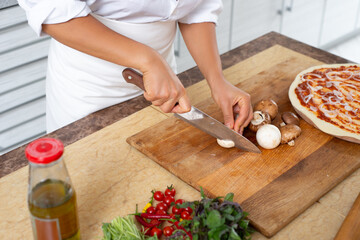 View of the hands of the chef slicing mushrooms on a wooden board.