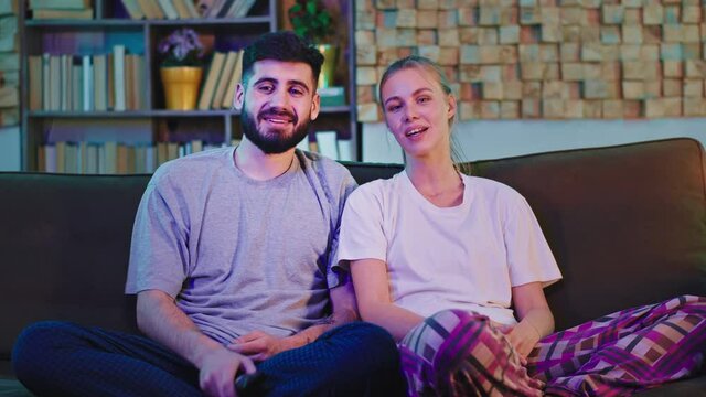 Young couple on the sofa at home in living room watching tv in front of the camera they discussing and smiling together. Shot on ARRI Alexa Mini