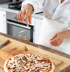 View of the hands of the chef throwing mushrooms on the pizza surface. Cooking vegan pizza.