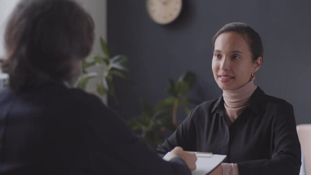 Beautiful mixed race woman sitting at office table with HR manager, looking at camera and smiling while posing during job interview