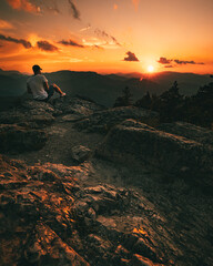 Obraz premium Hiker with backpack sitting on mountain and enjoying sunset