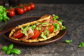 Pancake, omelet with ham, salad and tomatoes on a concrete background.