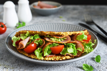 Pancake with ham, salad and tomatoes on a concrete gray background. Breakfast on the kitchen table.