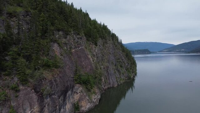 Drone flying by a rock cliff by a lake