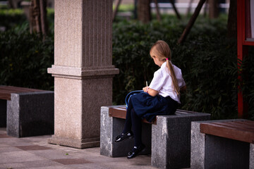 Back to school. Little girl from elementary school outdoor. Kid doing homework outdoor after lessons