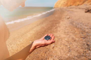 Hand holding a compass with a view of the sand and the sea