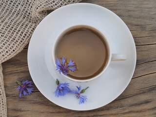 Herbal tea in a white сup with a saucer and flowers of a useful plant blue cornflower with a napkin on a wooden stand, top view. Medical herb centaurea cyanus with blue flowers for use in medicine