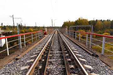 Railway bridge with rails extending into the distance against the background of an autumn forest