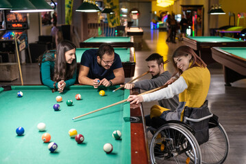 Fototapeta na wymiar Disabled girl in a wheelchair playing billiards with friends